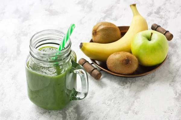 新鮮な健康的なキウイ ほうれん草 緑のリンゴとバナナスムージーグラスマソン瓶の中に灰色のコンクリートの背景にわら ストックフォト
