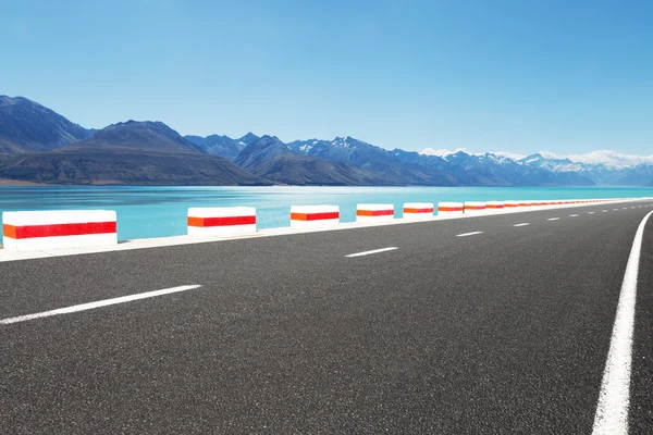 Asphalt road near water and snow mountains — Stock Photo, Image