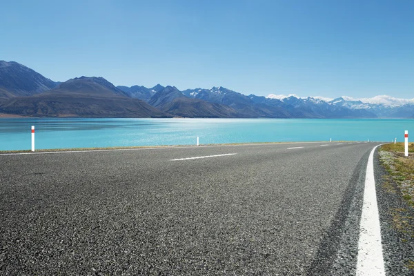 Empty asphalt road near water and snow mountains — Stock Photo, Image