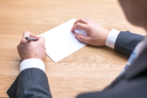 Businessman writing on white paper on table — Stock Photo, Image