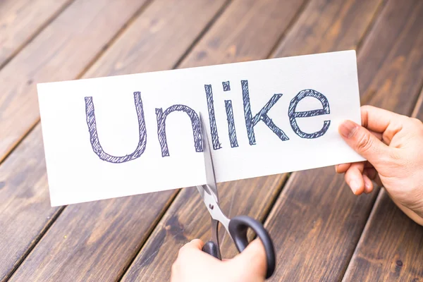 Woman holds paper with word unlike by scissors — Stock Photo, Image