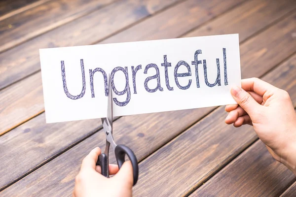 Woman cuts paper with word ungrateful — Stock Photo, Image