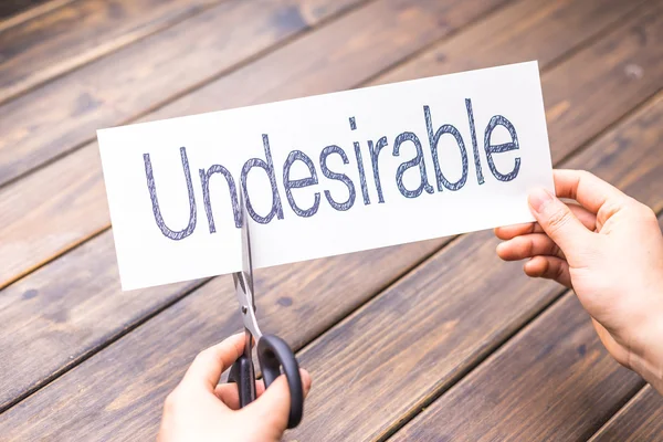 Woman cuts paper with word undesirable — Stock Photo, Image