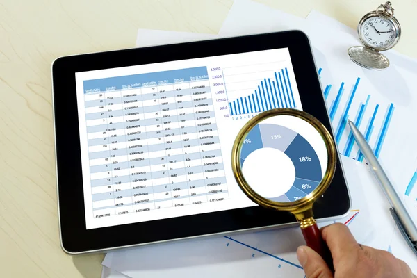 Hand with magnifying glass above the tablet  with financial chart report — Stock Photo, Image