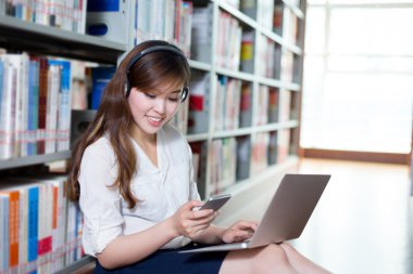 female student using laptop and mobile phone in library clipart