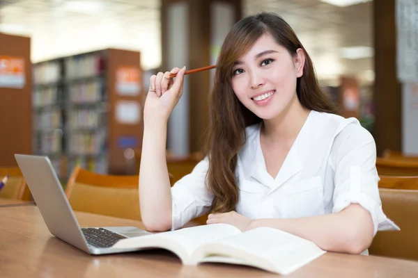 Female student studying in library with laptop — Stock Photo, Image