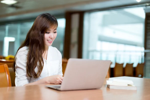 Kvinnlig student som studerar i biblioteket med laptop — Stockfoto