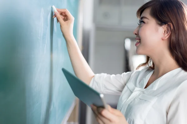 Asian woman holding tablet and writing on blackboard — Stock Photo, Image
