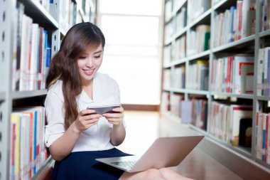 kız öğrenci dizüstü bilgisayar ve cep telefonu Kitaplığı'nda kullanma