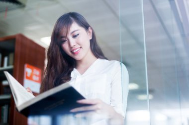 Asyalı kız öğrenci holding kitap kütüphane 