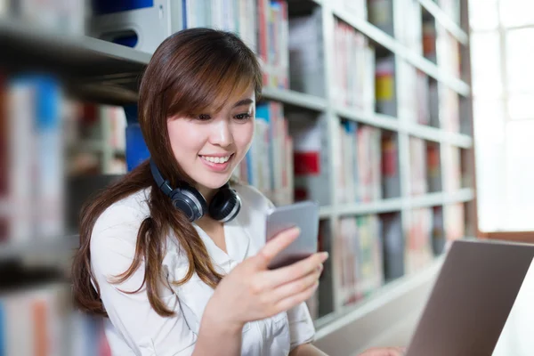 Kvinnlig student med laptop och mobiltelefon i biblioteket — Stockfoto