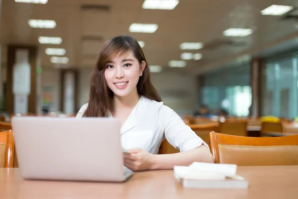 Kvinnlig student som studerar i biblioteket med laptop — Stockfoto