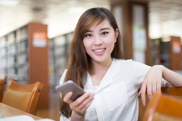 Vrouwelijke student gebruik mobiele telefoon in de bibliotheek — Stockfoto