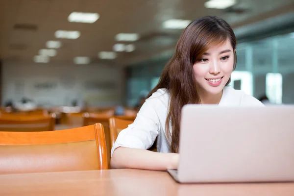 Vrouwelijke student studeren in de bibliotheek met laptop — Stockfoto