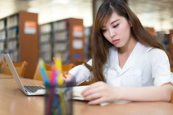 Female student studying in library with laptop — Stock Photo, Image