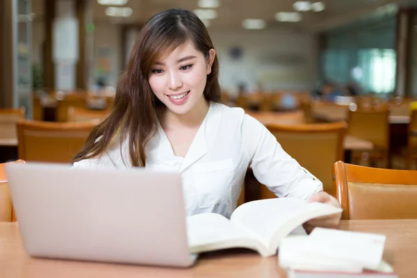 Θηλυκό φοιτητής που σπουδάζει στη βιβλιοθήκη με φορητό υπολογιστή — Φωτογραφία Αρχείου