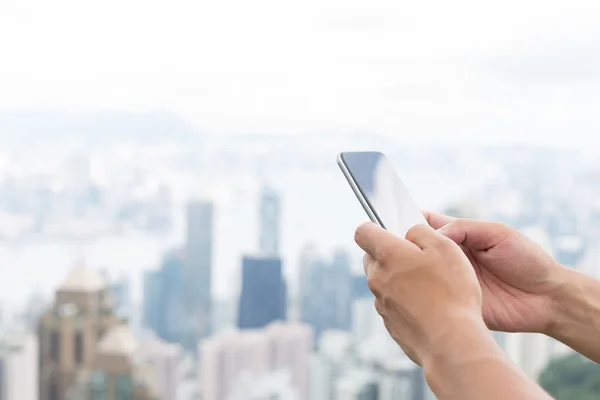 Mano celebración de teléfono móvil con paisaje urbano como fondo —  Fotos de Stock