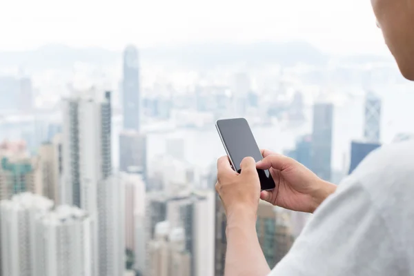 Mano celebración de teléfono móvil con paisaje urbano como fondo — Foto de Stock