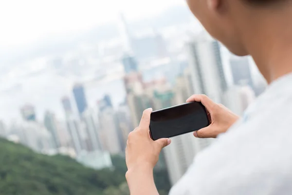 Hand hält Handy mit Stadtbild als Hintergrund — Stockfoto