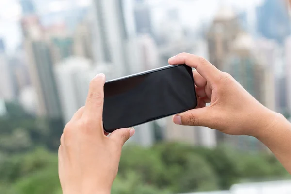 Рука держит мобильный телефон с городским пейзажем в качестве фона — стоковое фото