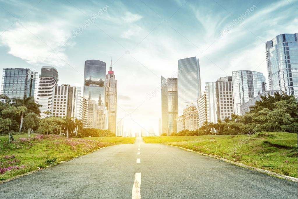 asphalt road and skyscrapers under sunbeam