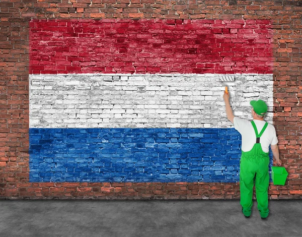 Malíř maluje vlajka Hetherlands na zeď — Stock fotografie