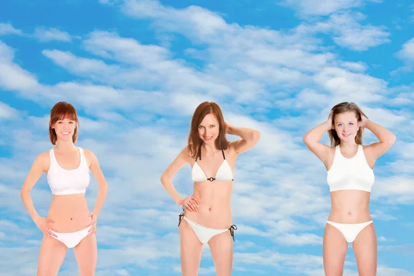 白い雲と青い夏の空の前にビキニを着た3人の若い女性の肖像 — ストック写真