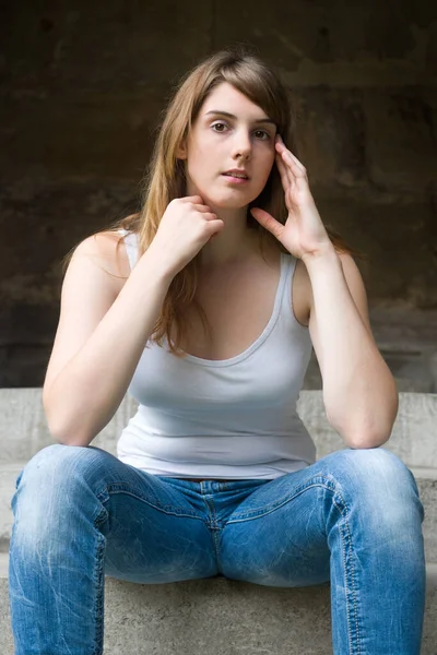 暗い壁の前の階段に座って魅力的な若い女性の屋外の肖像画 — ストック写真