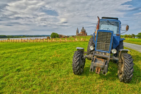 Viejo tractor oxidado en un campo con monasterio en el fondo —  Fotos de Stock