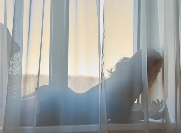 Jolie rousse fille couchée derrière des rideaux sur une fenêtre en sh sexy — Photo