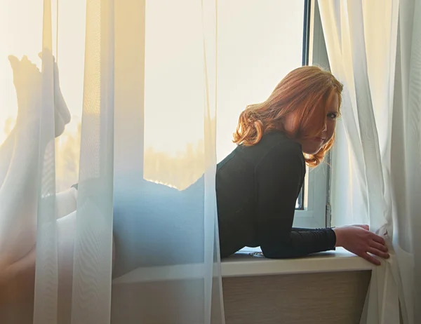 Jolie rousse fille couchée derrière des rideaux sur une fenêtre en sh sexy — Photo