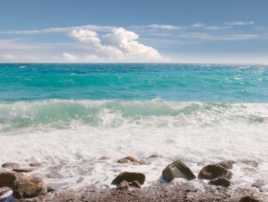 Çakıl taşlı deniz plajı ve ufukta güneşli gökyüzü.