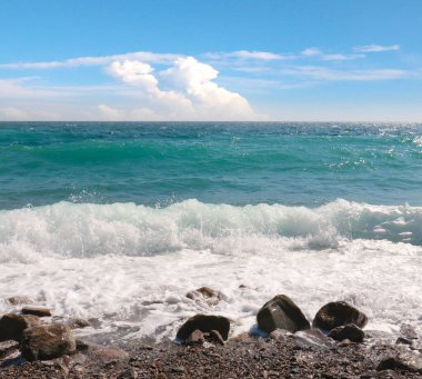Çakıl taşlı deniz plajı ve ufukta güneşli gökyüzü.
