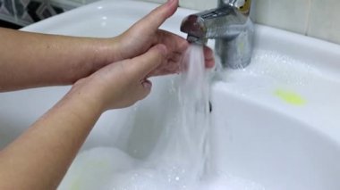 Adam ellerini temiz suyun altında yıkar.