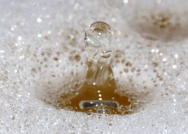 a drop of clean water falls on the surface of a dirty liquid with foam