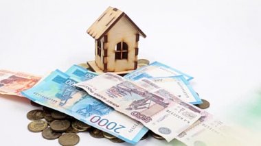 Kağıt ruble banknotları, ipoteğin sembolü olarak ahşap bir evin yanındaki masa yüzeyine düşer.