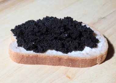 Bir dilim tereyağlı beyaz çavdar ekmeği ve bir demet siyah mersin balığı havyarı.