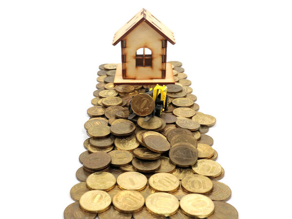 a wooden house and a plastic model of a tractor stand on a pile of Russian rubles