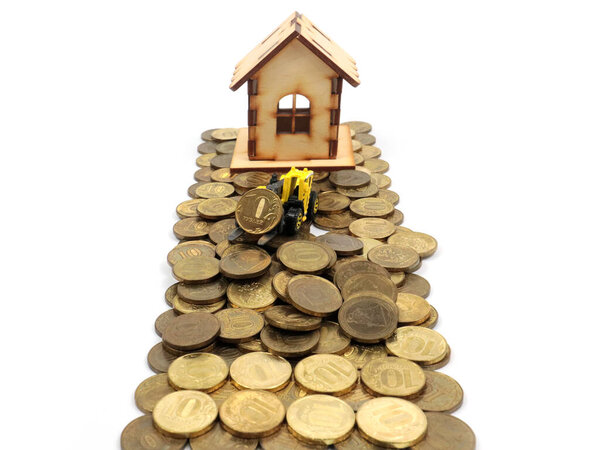 a wooden house and a plastic model of a tractor stand on a pile of Russian rubles