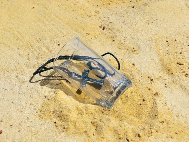 Değerli taşlarla süslenmiş bir haç ve kumun üzerinde boş bir bardak kaçınılmazlığın sembolü olarak.