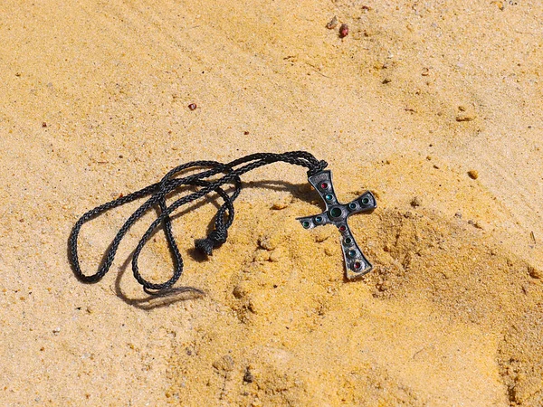 religious symbol cross with jewelry with precious stones lies on the sand