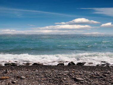 Deniz dalgaları bulutlu bir gökyüzünün altındaki çakıl taşı plajına düşüyor.