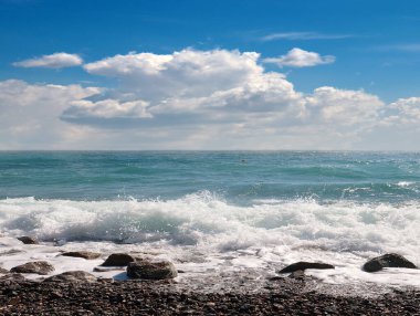 Deniz dalgaları bulutlu bir gökyüzünün altındaki çakıl taşı plajına düşüyor.