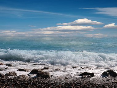 Deniz dalgaları bulutlu bir gökyüzünün altındaki çakıl taşı plajına düşüyor.