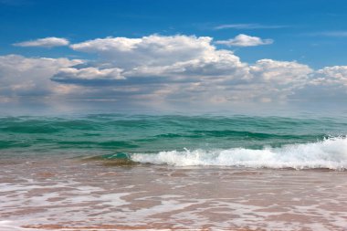 Bulutlu, güneşli bir gökyüzünün altında güzel bir sahil.