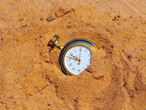 antique pocket watch lies in the sand as part of the passage of time