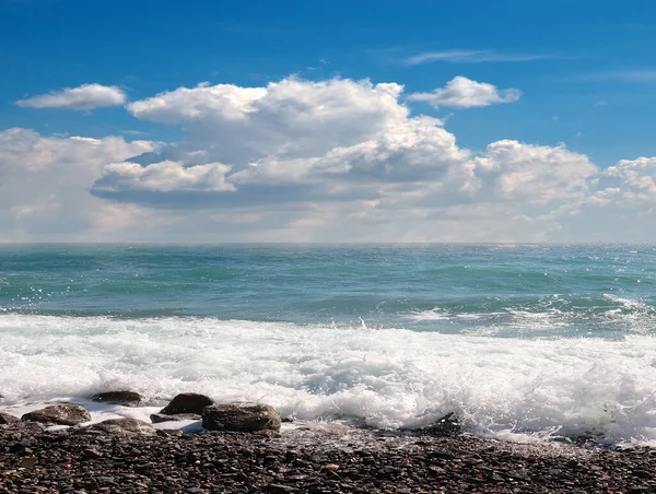 海の波は雲の多い空の下の小石のビーチに落ち — ストック写真