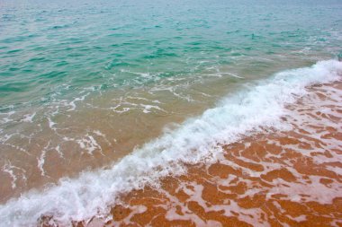 Deniz dalgasının yüzeyinde köpük ve hava kabarcıkları ve kumsalın kumlu kıyıları.