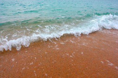 Deniz dalgasının yüzeyinde köpük ve hava kabarcıkları ve kumsalın kumlu kıyıları.