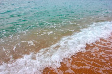 Deniz dalgasının yüzeyinde köpük ve hava kabarcıkları ve kumsalın kumlu kıyıları.